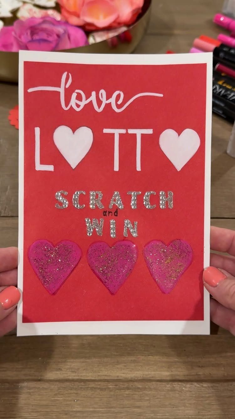 Handmade red love lotto scratch-off card with pink glitter hearts held by hands.