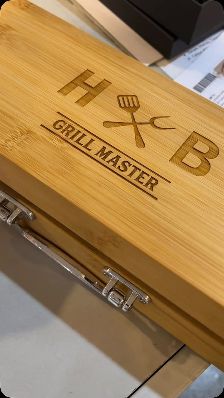 Engraved wooden grill master box with initials H and B and cooking utensils.