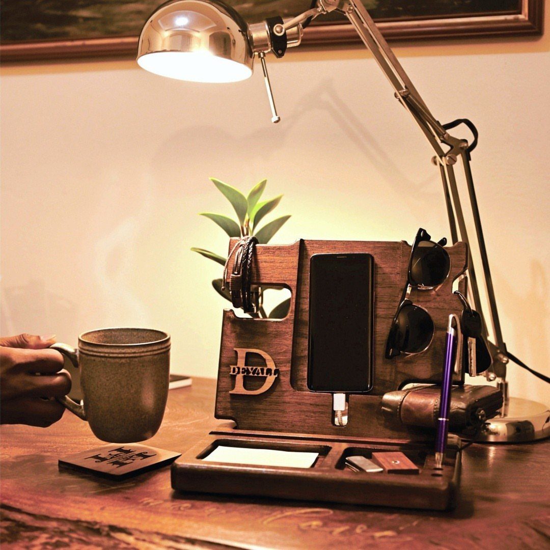 Wooden docking station holding a phone, sunglasses, and watch on a lit desk.