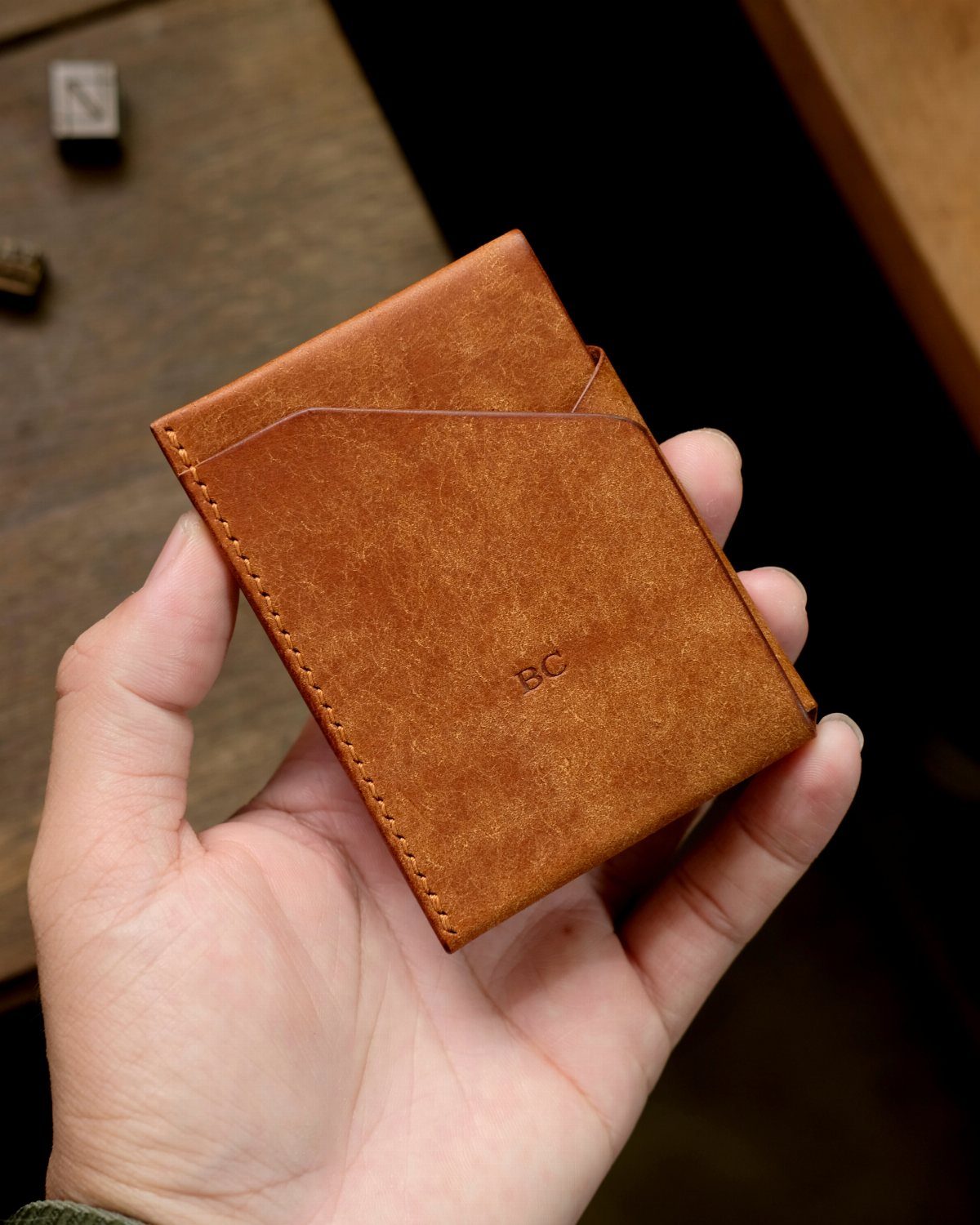 Brown leather wallet with embossed initials held in a person's hand.