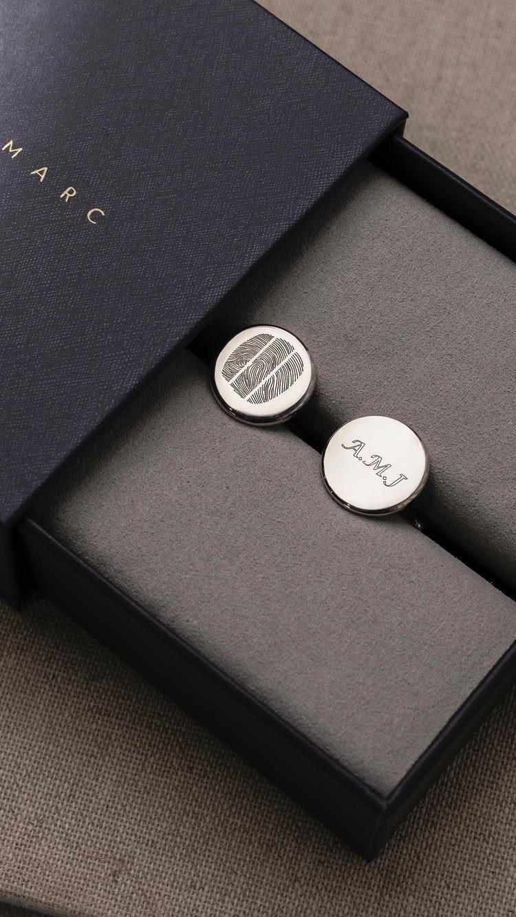 Silver cufflinks with fingerprint and initial engravings in a dark blue gift box.