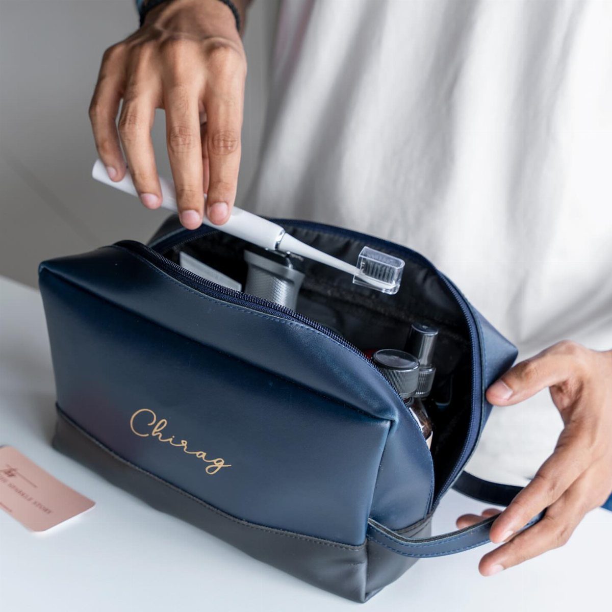 Navy blue leather toiletry bag with gold personalized name containing grooming supplies.