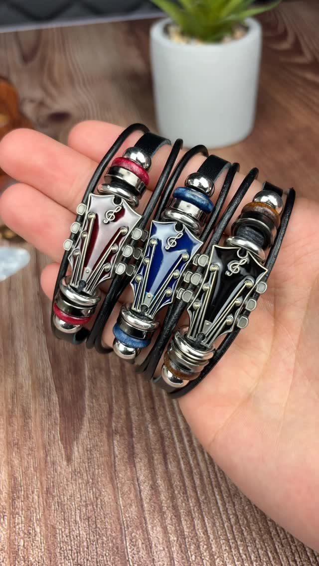 Three leather bracelets with guitar headstock charms held in a person's hand.