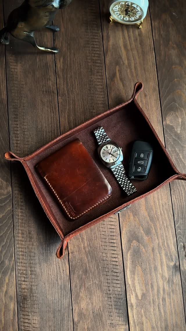 Leather valet tray holding a wallet, silver wristwatch, and car key on wood.