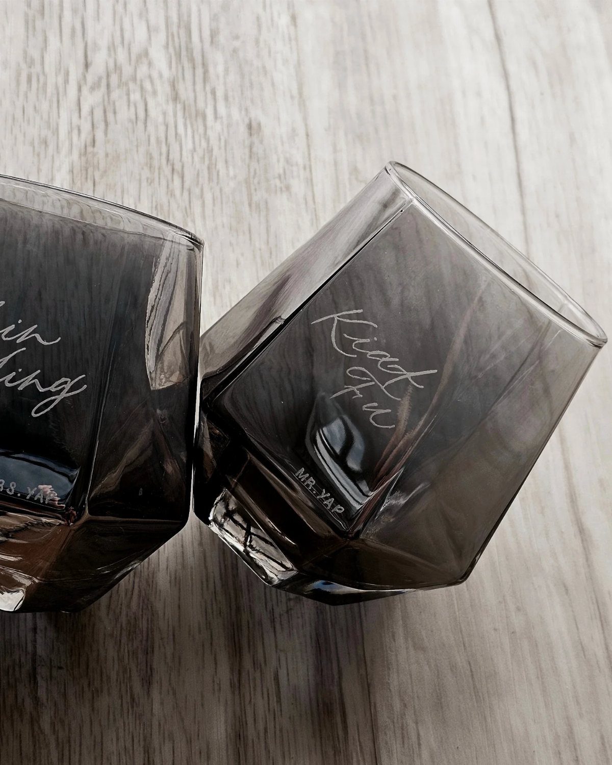 Two grey glass tumblers with personalized etched names on a wooden table