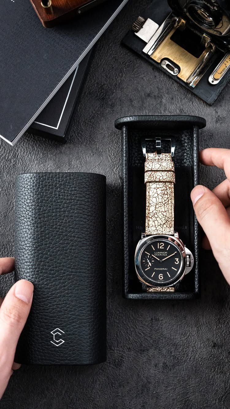 Black leather travel watch roll holding a wristwatch with a light-colored strap.