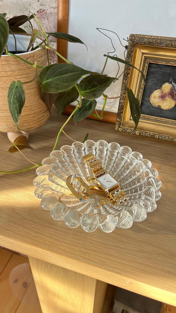 Gold watch inside a clear fluted glass bowl on a wooden table