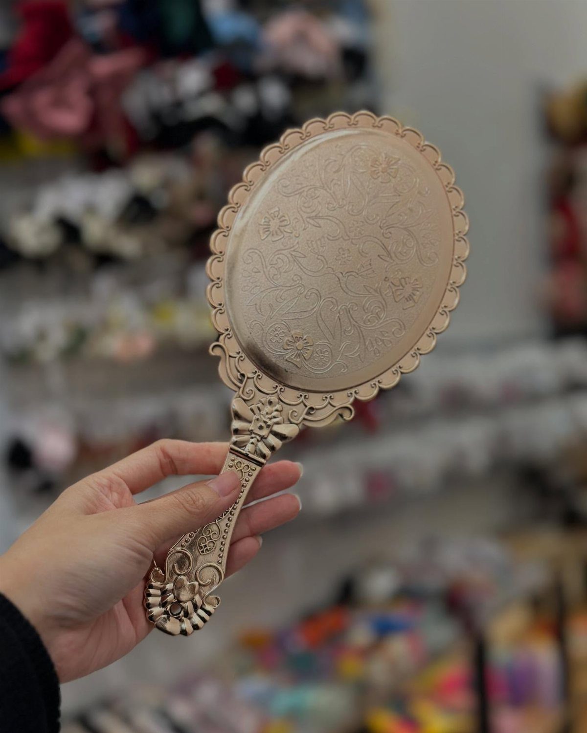 Ornate gold-toned vintage hand mirror with floral engravings held by a hand.
