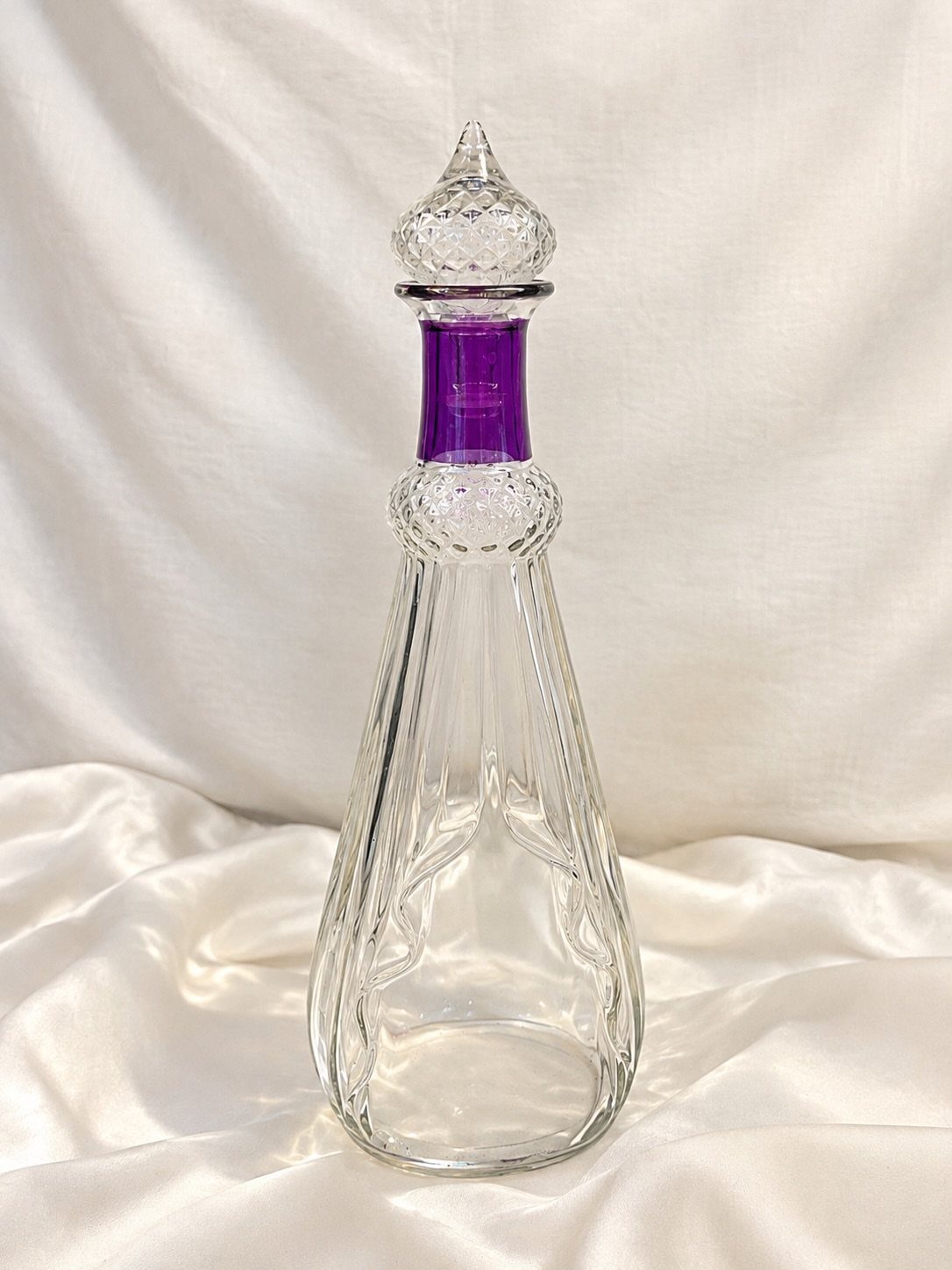 Vintage glass decanter with a purple neck band on white satin fabric