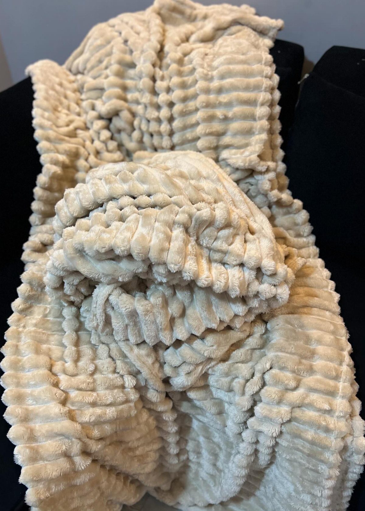 Cream-colored plush ribbed blanket folded on a dark black surface.