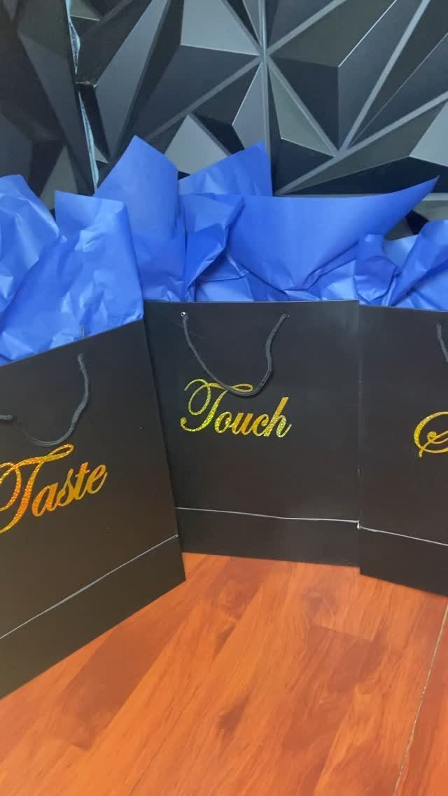 Black gift bags with gold text and blue tissue paper on wooden floor
