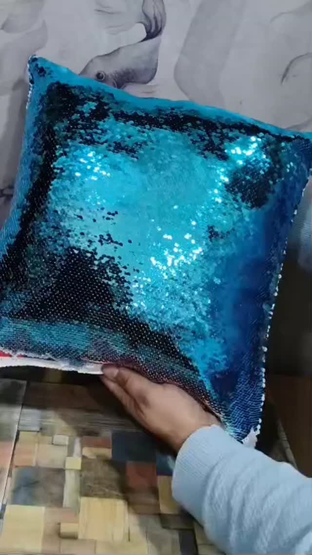 Blue sequin pillow held by a hand against a patterned wall background