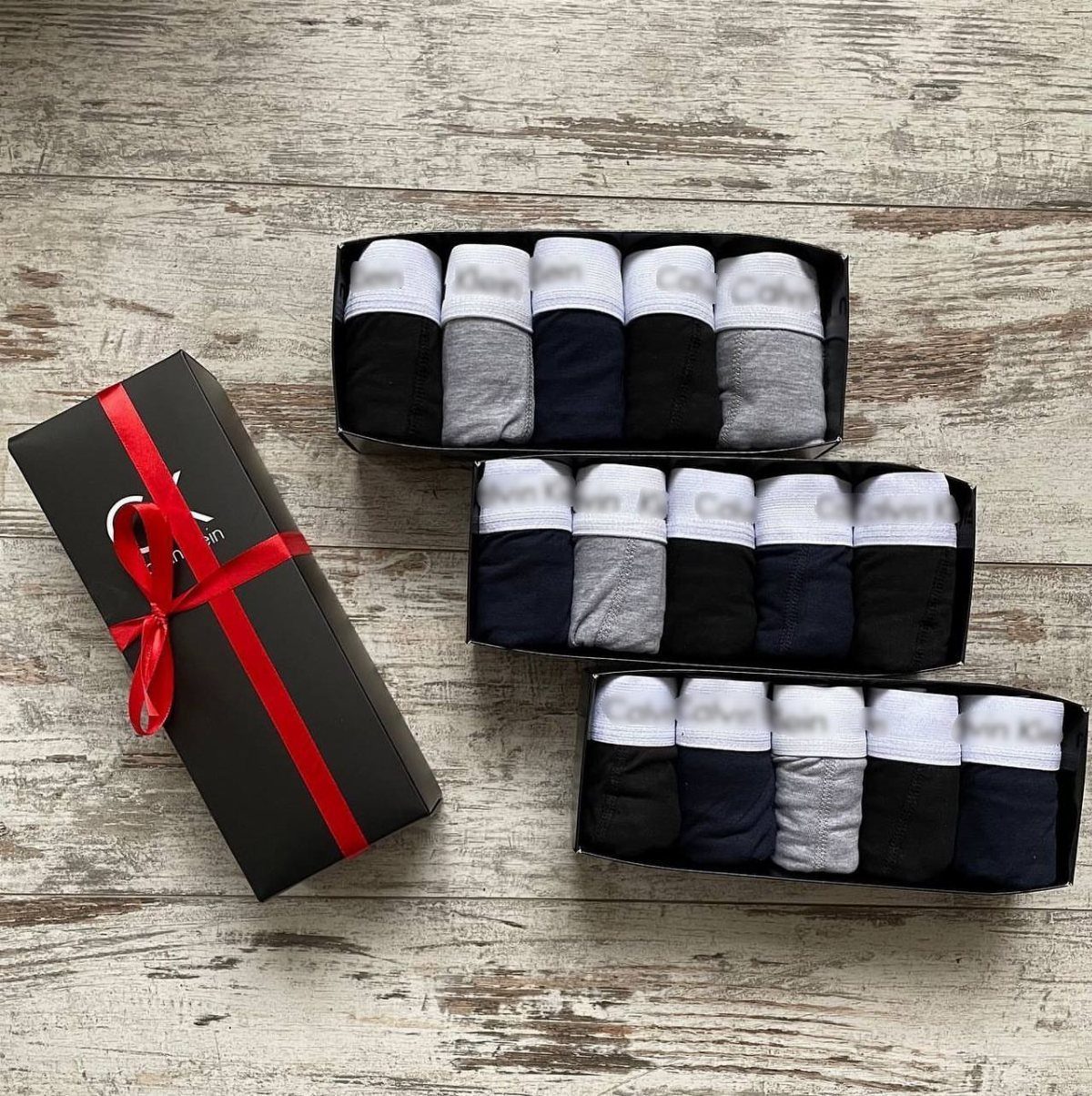 Folded men's underwear in black and grey boxes with a red ribbon gift box.