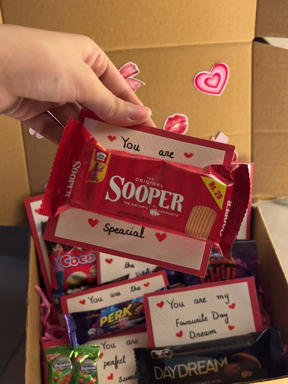 Hand holding a personalized candy wrapper in a gift box of sweets.