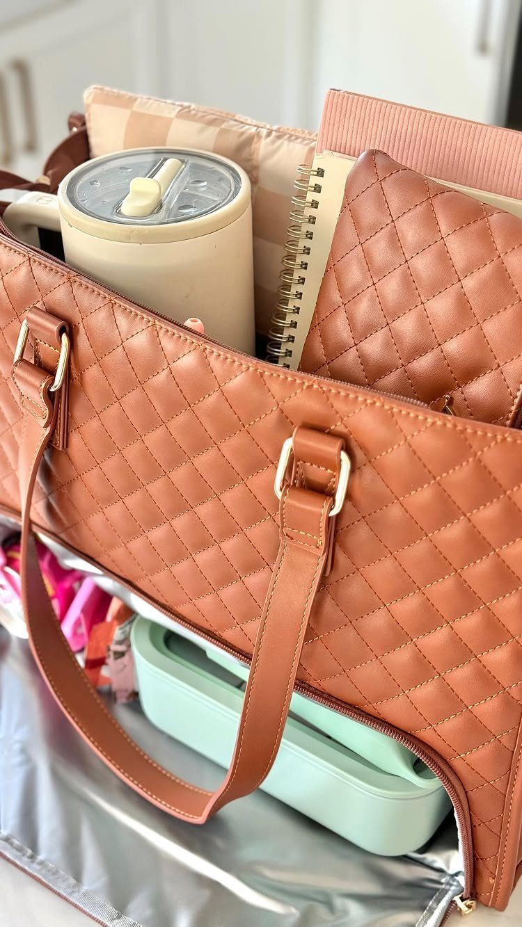 Brown quilted lunch bag containing a tumbler, notebook, and green food container.