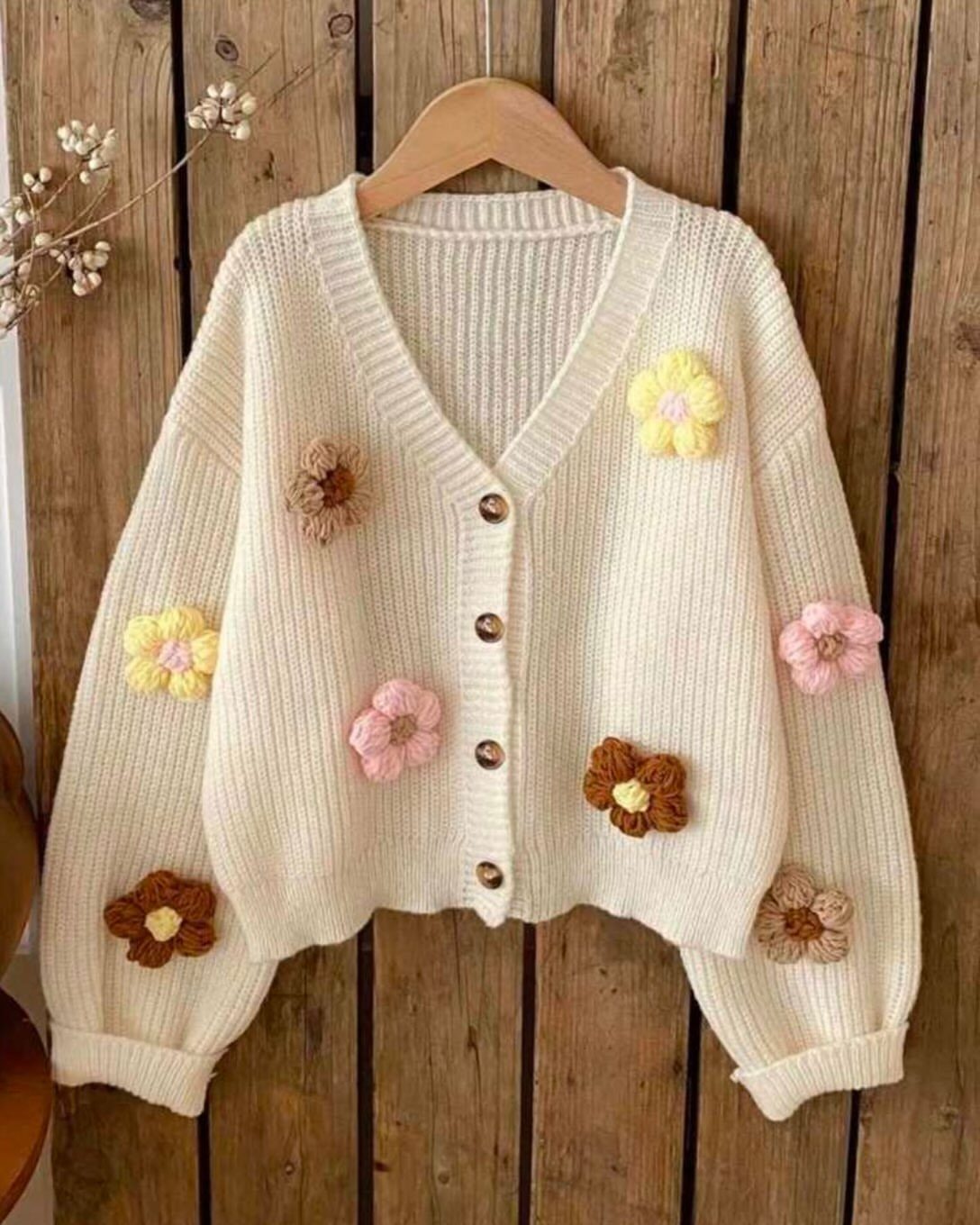 Cream ribbed knit cardigan with colorful 3D flower appliques on a wooden hanger