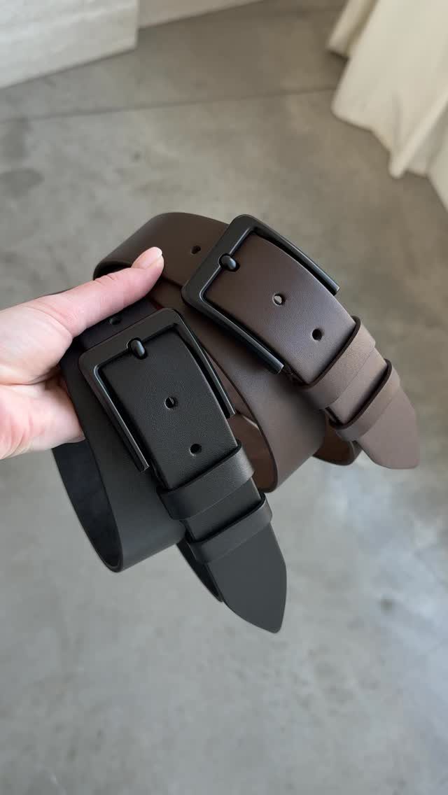 Black and brown leather belts with buckles held in a person's hand.