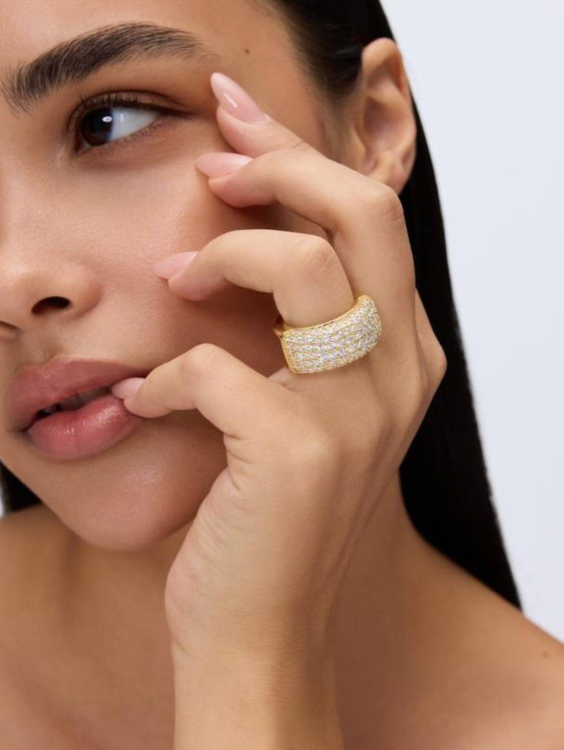 Woman wearing a wide gold ring with crystals on her finger