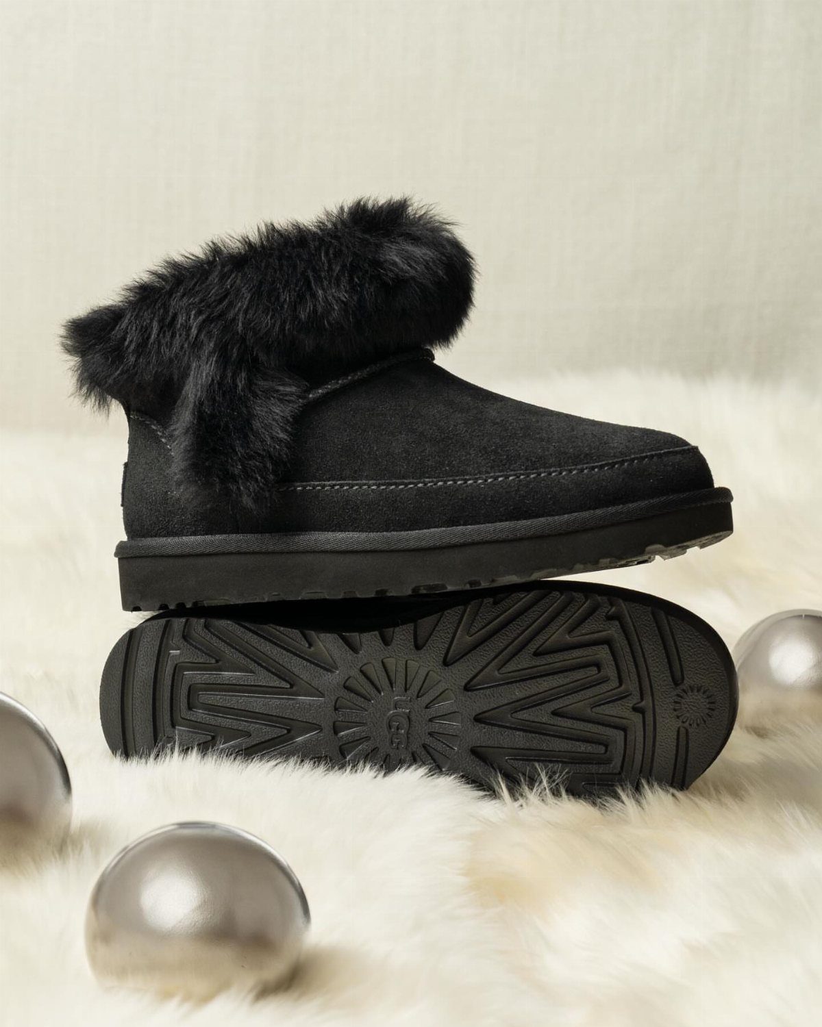 Black suede boots with faux-fur trim on a white fluffy rug with silver ornaments