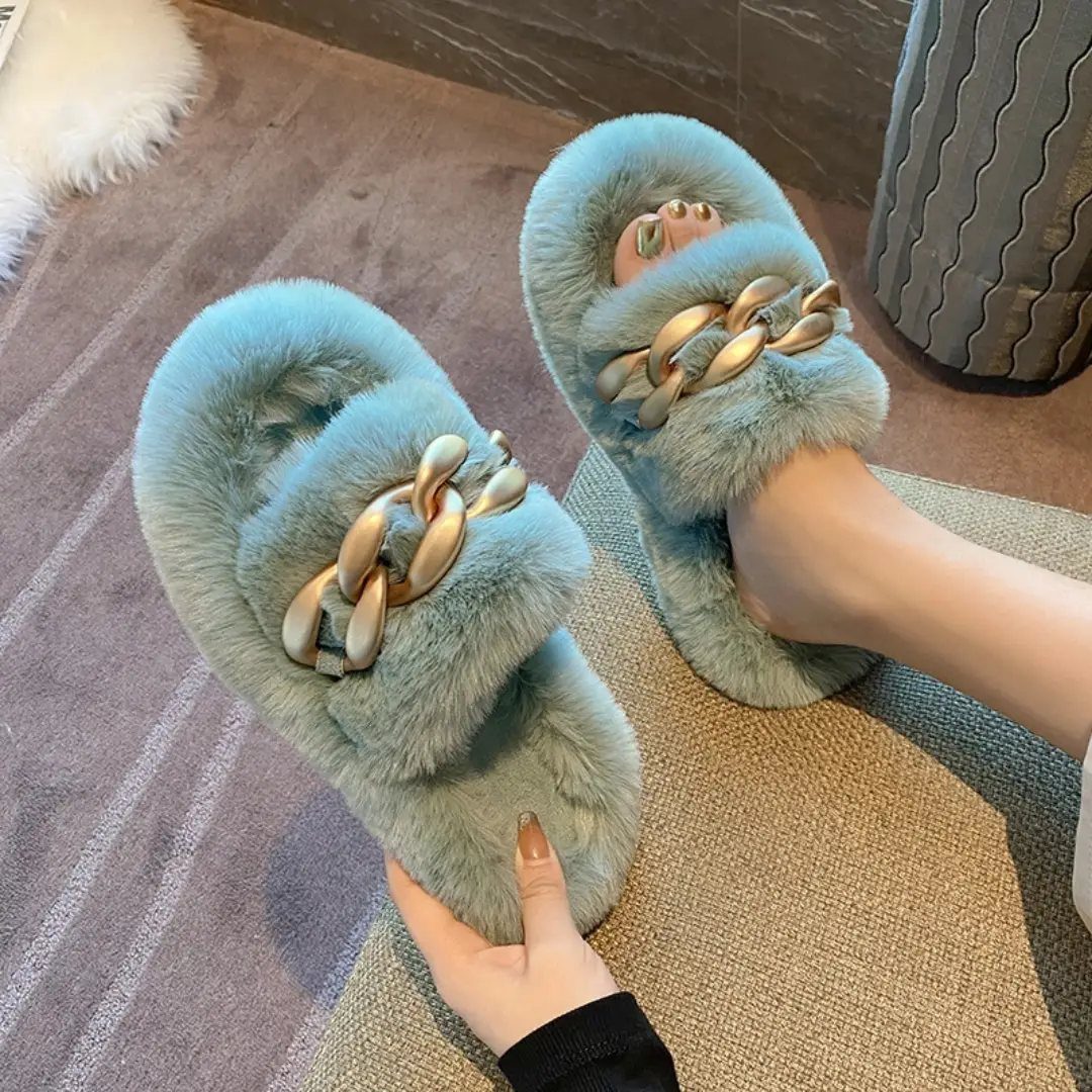 Light blue faux fur slippers with gold chain details on a grey rug