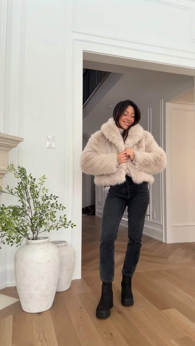 Woman wearing a fluffy beige faux fur jacket and black boots in a hallway