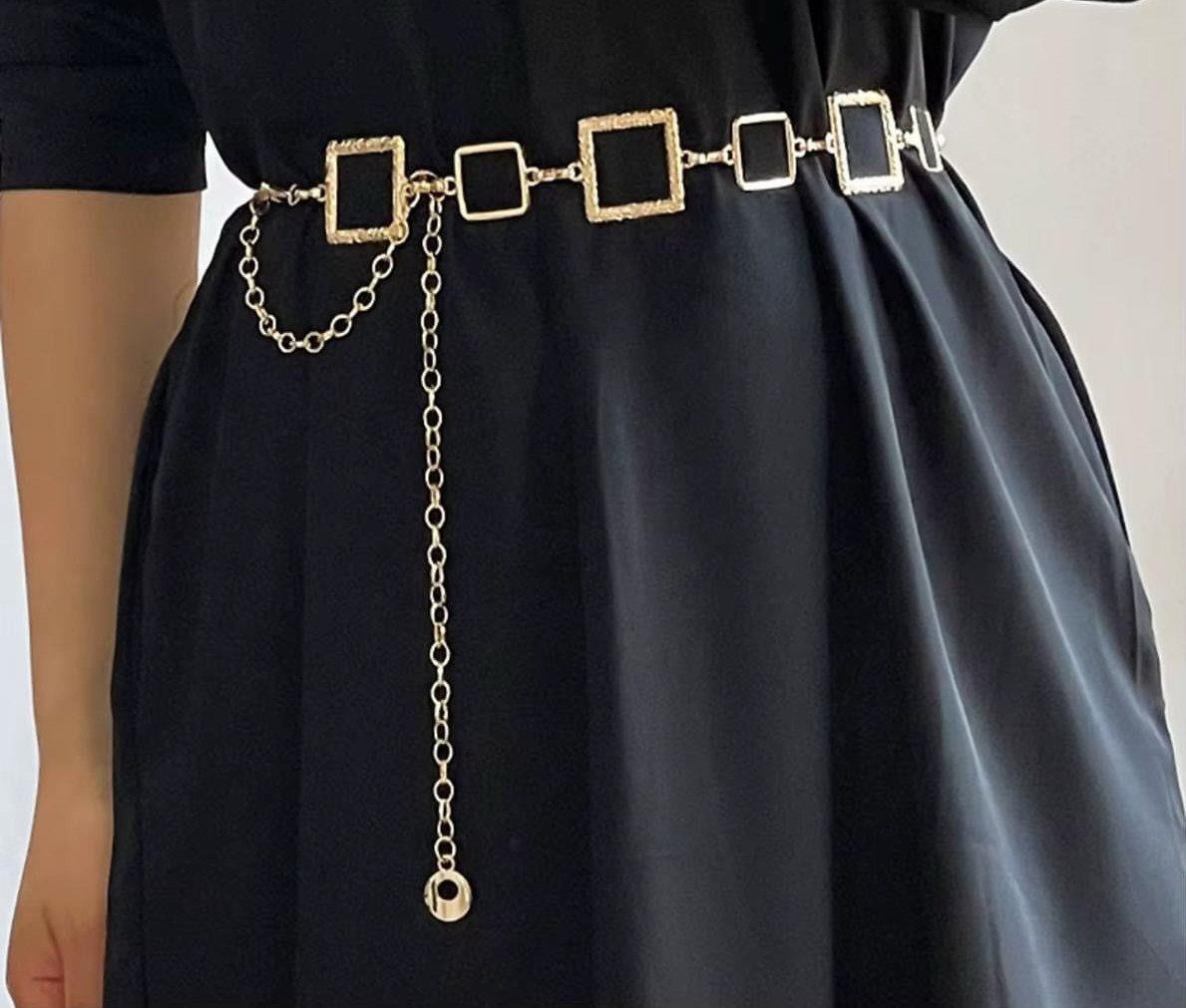 Gold metal chain belt with square links worn over a black dress