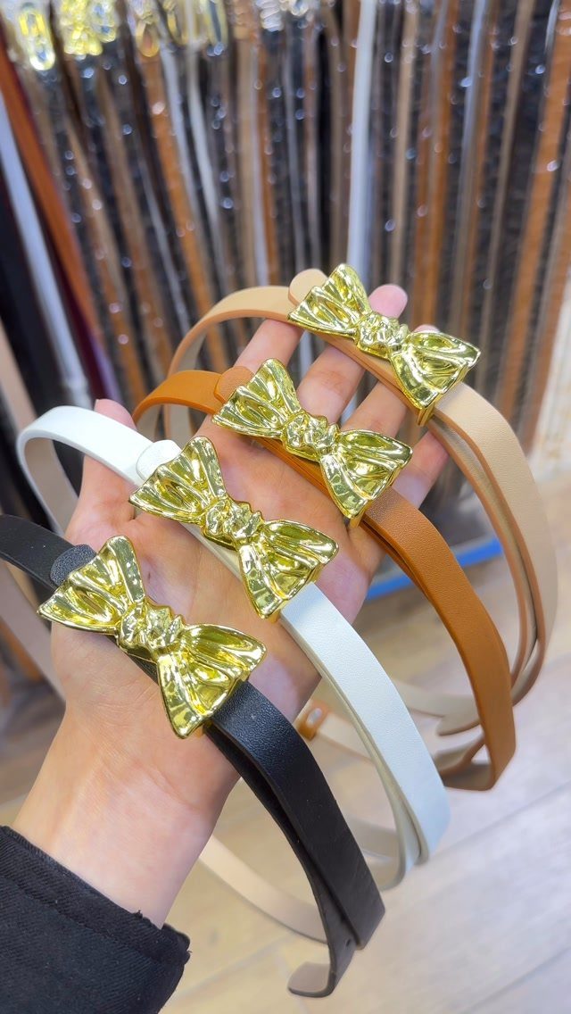 Four colorful headbands with gold metallic bows held in a person's hand.