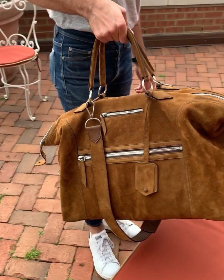 Brown suede duffel bag with silver zippers held by a person on brick patio