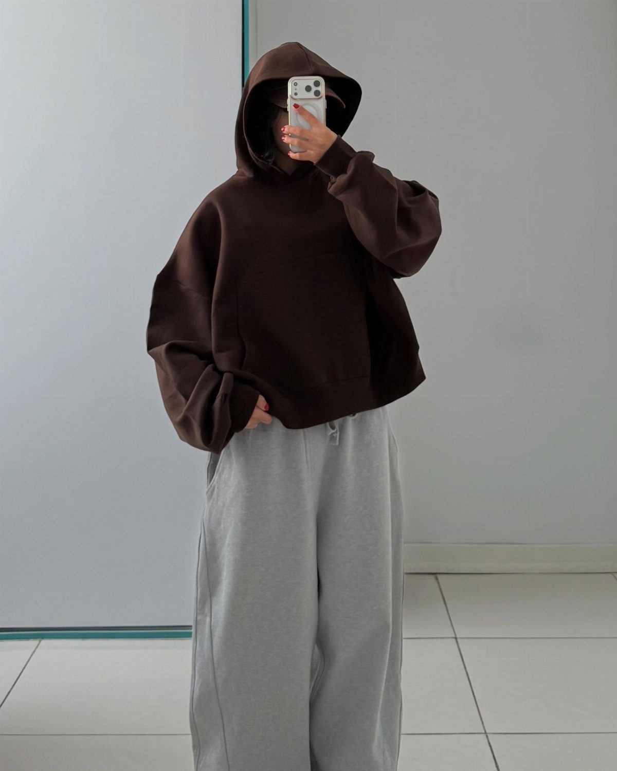 Person wearing an oversized brown hoodie and grey sweatpants taking a mirror selfie.
