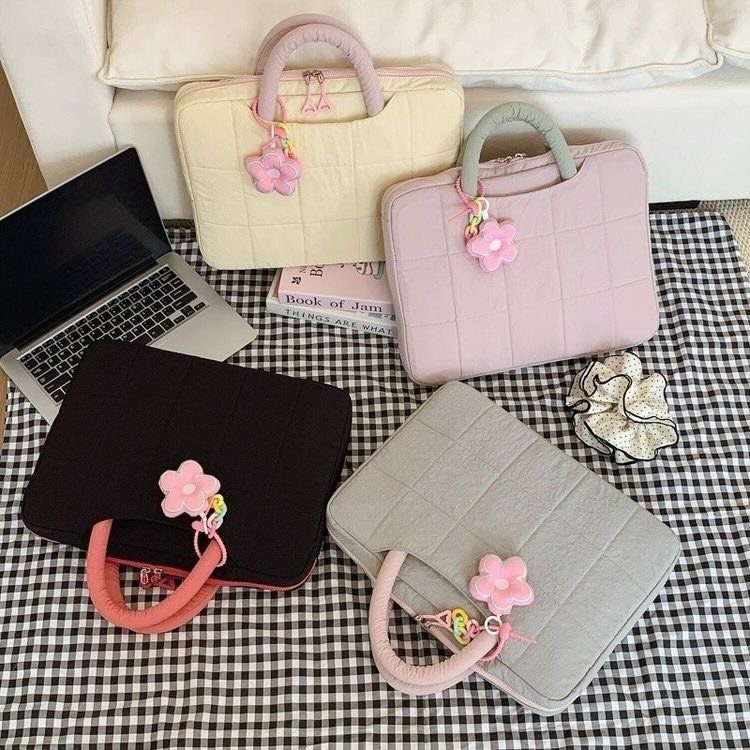 Quilted laptop sleeves in various colors with flower charms on checkered fabric.