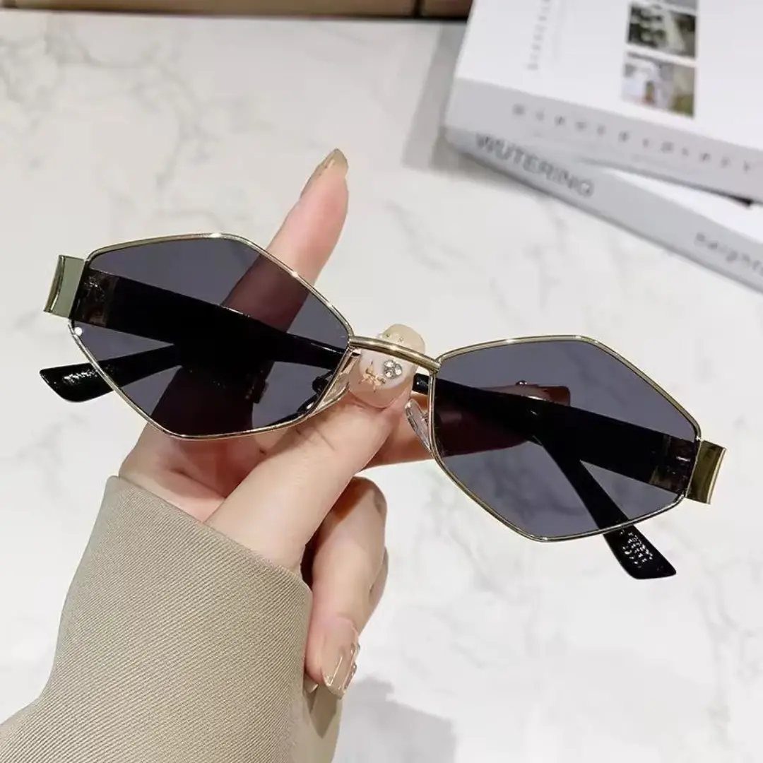 Gold-framed hexagonal sunglasses with dark lenses held by a hand over marble.