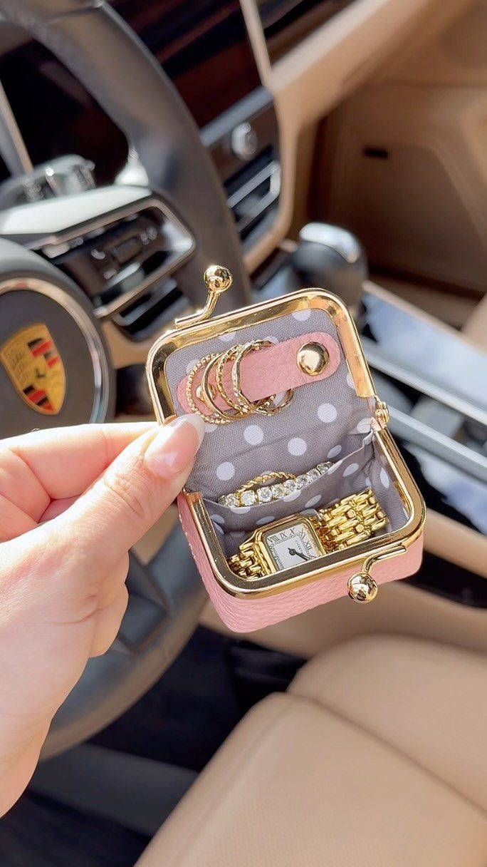 Small pink travel jewelry case holding a gold watch, bracelet, and rings.