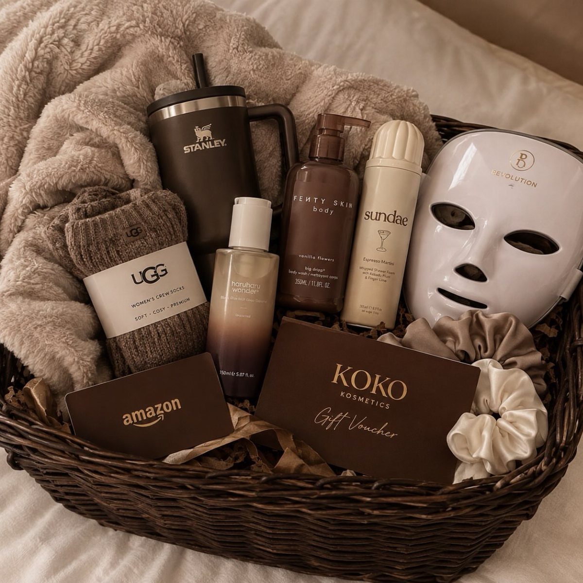 Wicker gift basket with beauty products, Ugg socks, and a Stanley tumbler