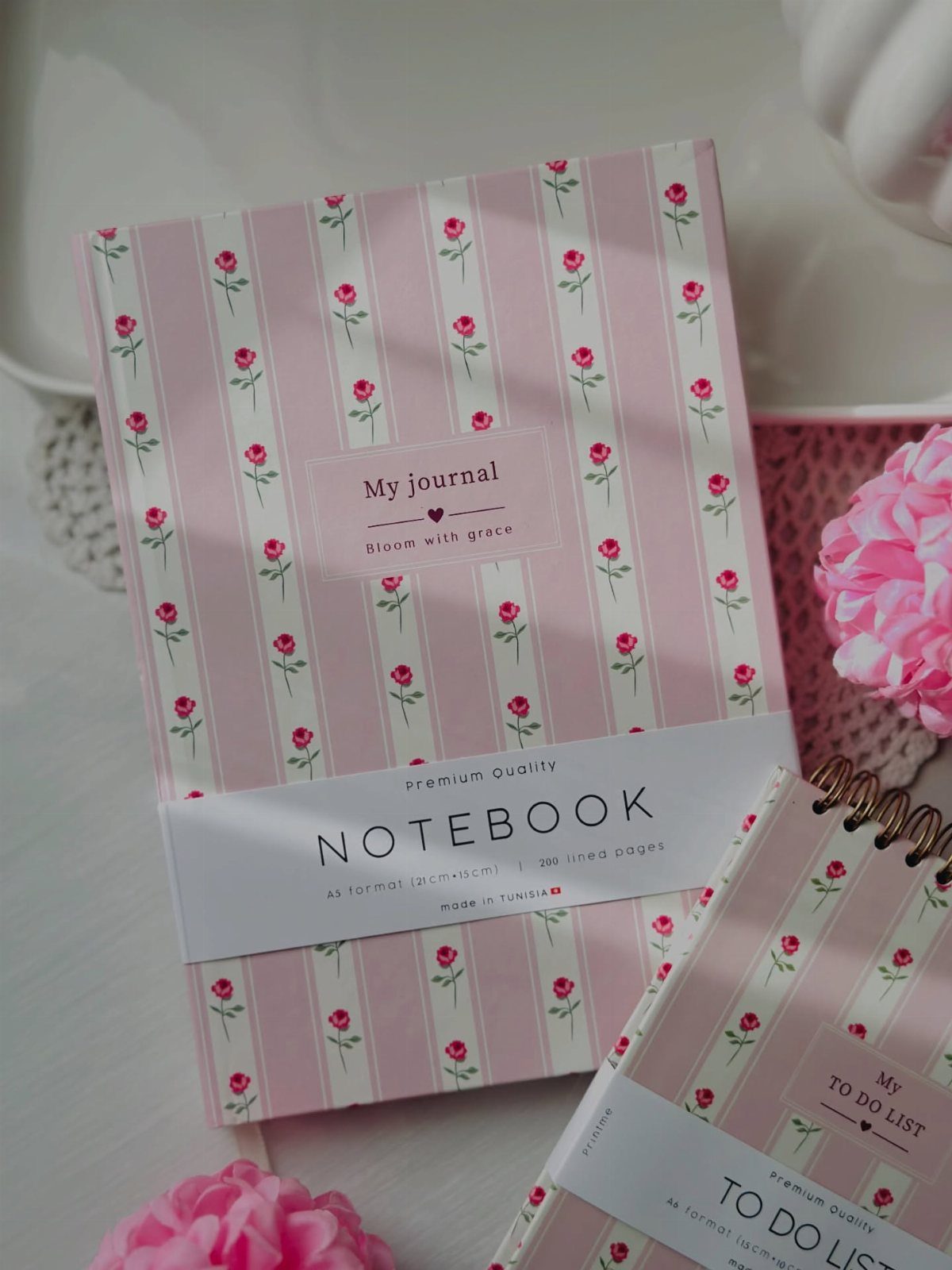 Pink striped notebooks with red rose patterns and white labels on white surface