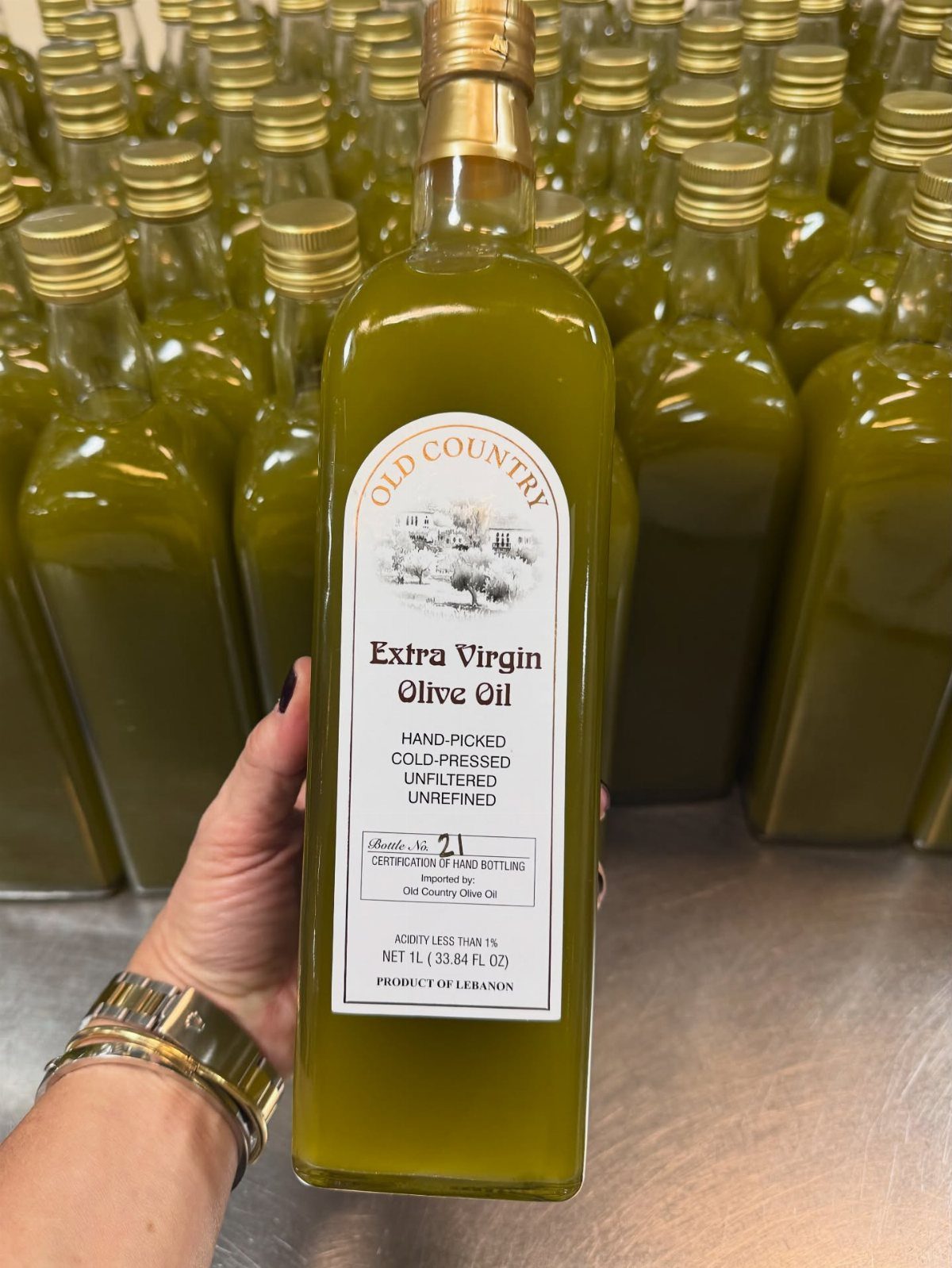 Bottle of extra virgin olive oil held in front of many other bottles.