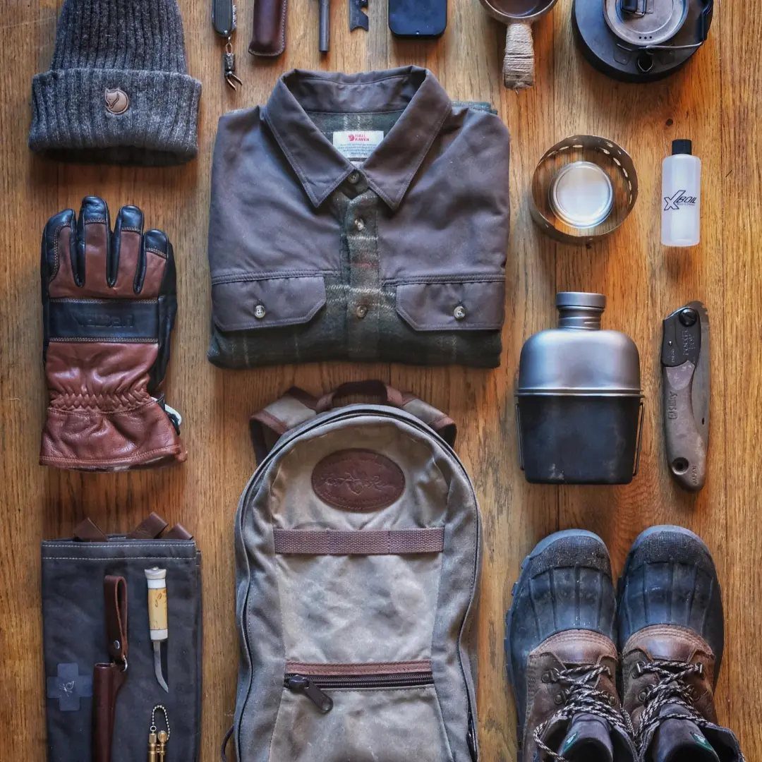 Outdoor gear flat lay with brown shirt, canvas backpack, boots, and metal flask.