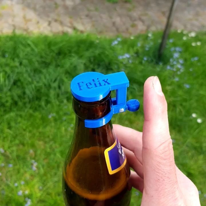 Brown beer bottle with a blue personalized bottle stopper held by a hand.