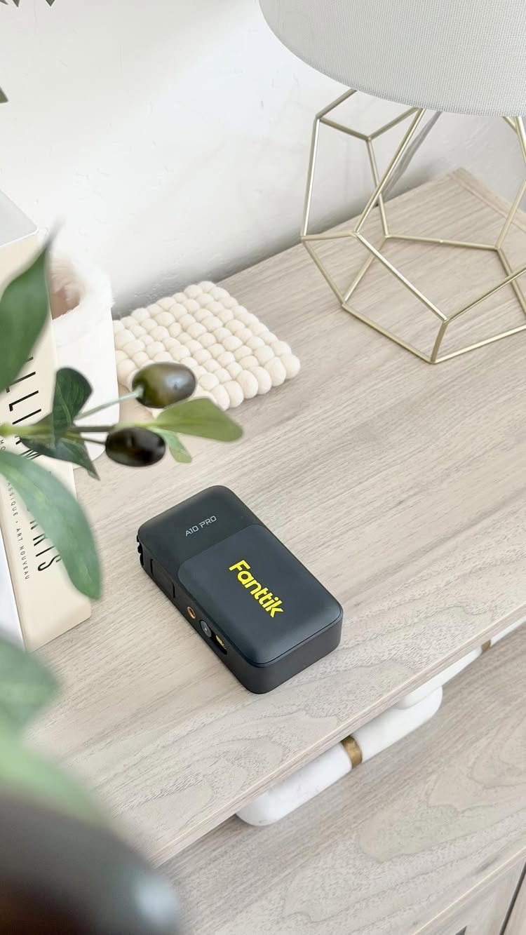 Black Fanttik electronic gadget on a light wooden table with a gold lamp.