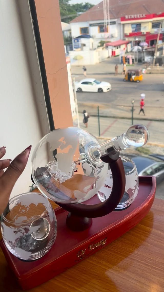 Globe-shaped glass whiskey decanter and glass on a red wooden tray by a window.