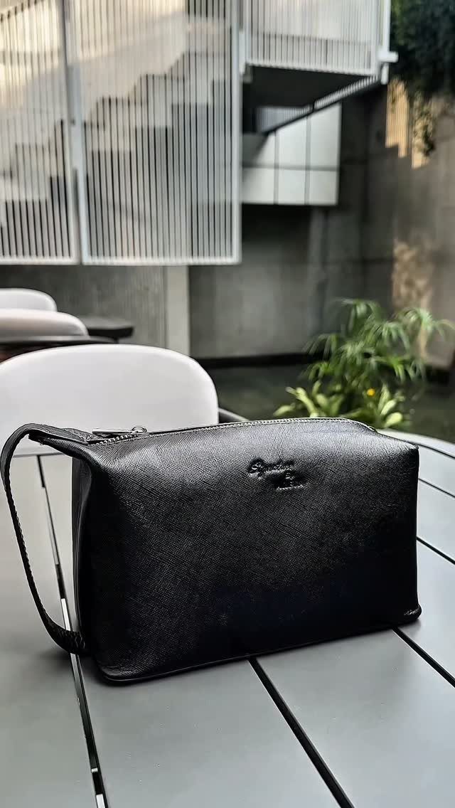 Black leather toiletry bag with handle sitting on a grey outdoor table