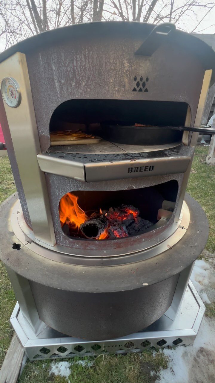 Outdoor pizza oven with a burning fire and pizza cooking inside.