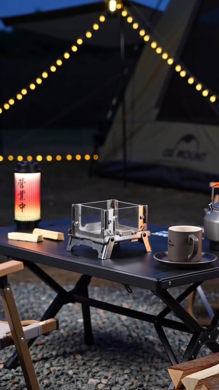 Camping gear including a portable stove and lantern on a black folding table.