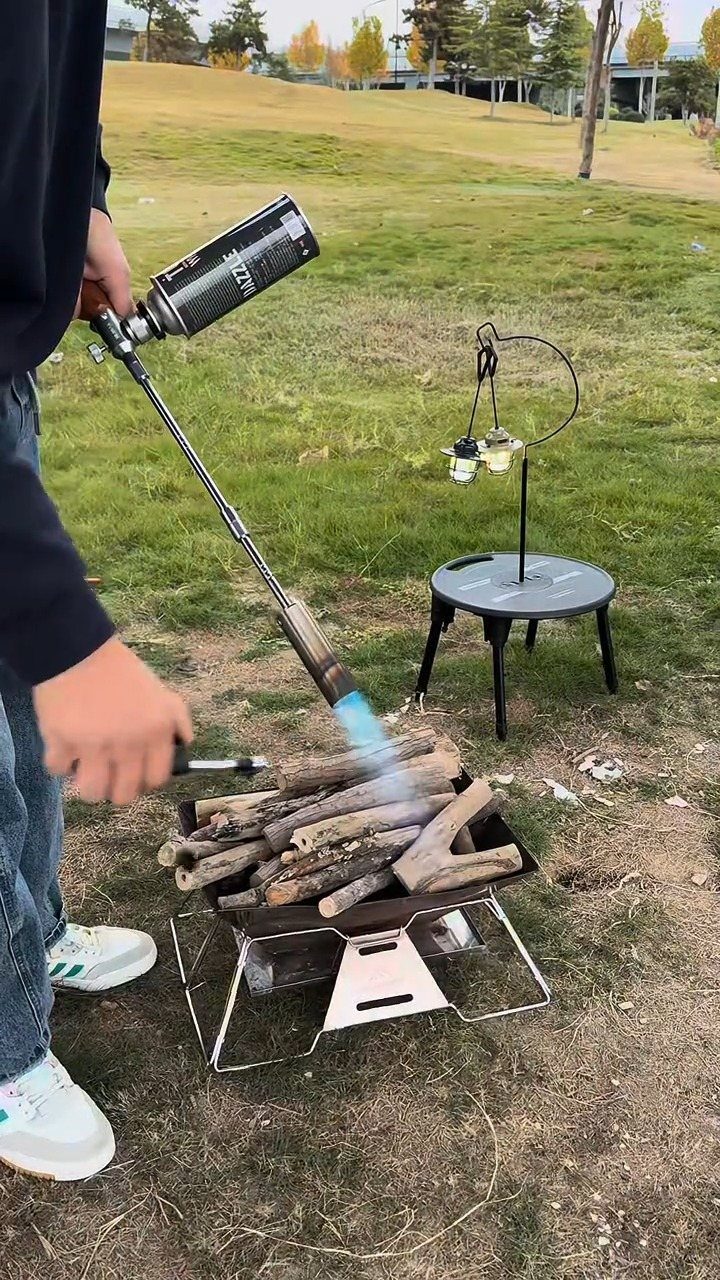 Person using a propane torch to start a fire in a portable pit