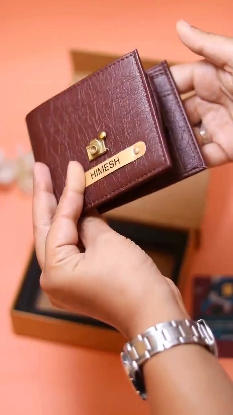 Brown leather wallet with engraved name plate held by hands over gift box