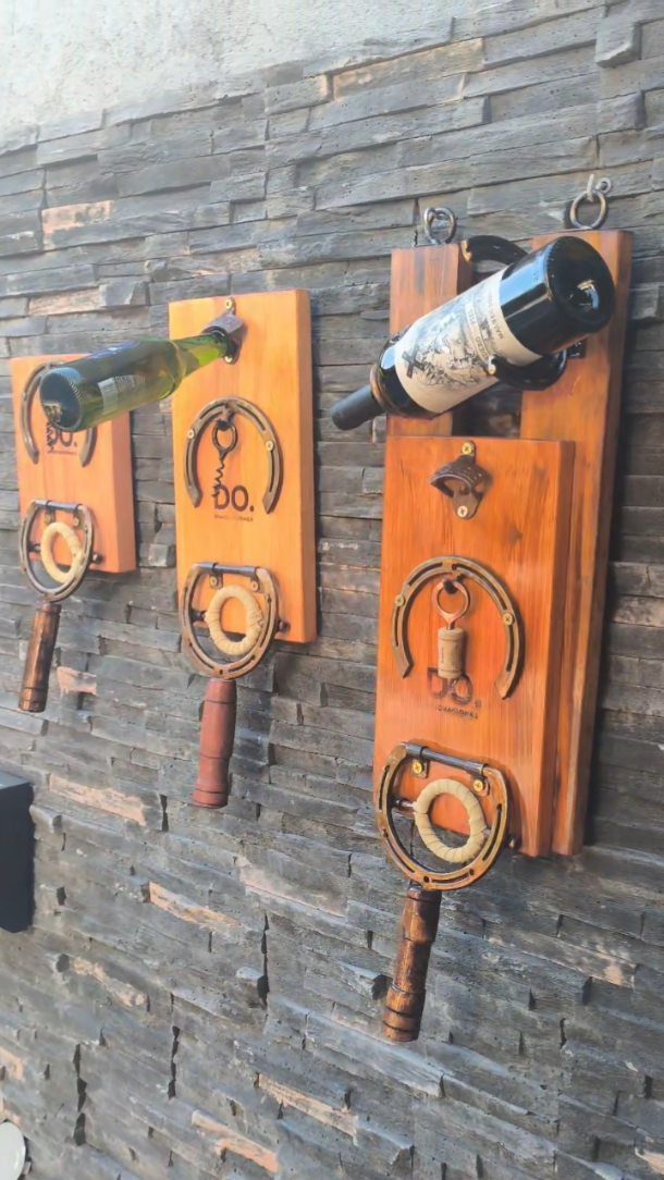 Wooden wine bottle holders with horseshoe accents mounted on a grey stone wall.