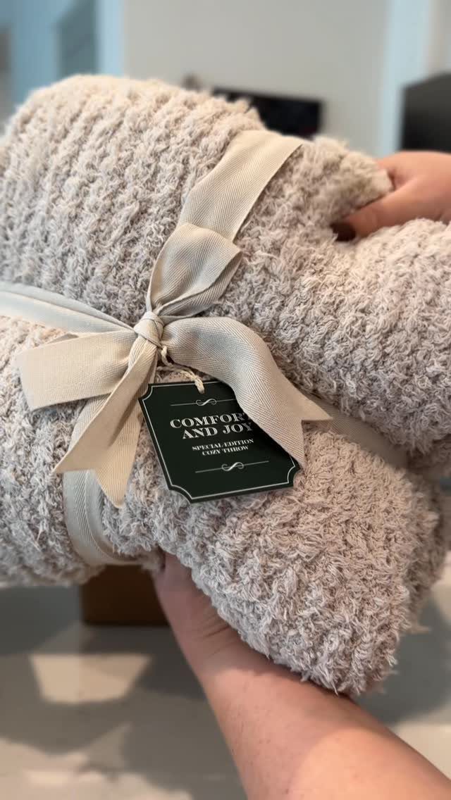 Beige fluffy blanket tied with a ribbon and a Comfort and Joy gift tag.
