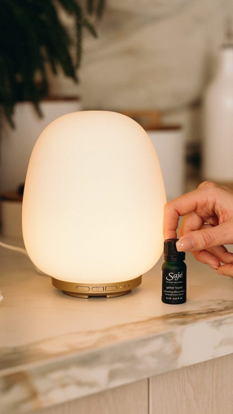 Glowing white essential oil diffuser and a small bottle on a marble surface.