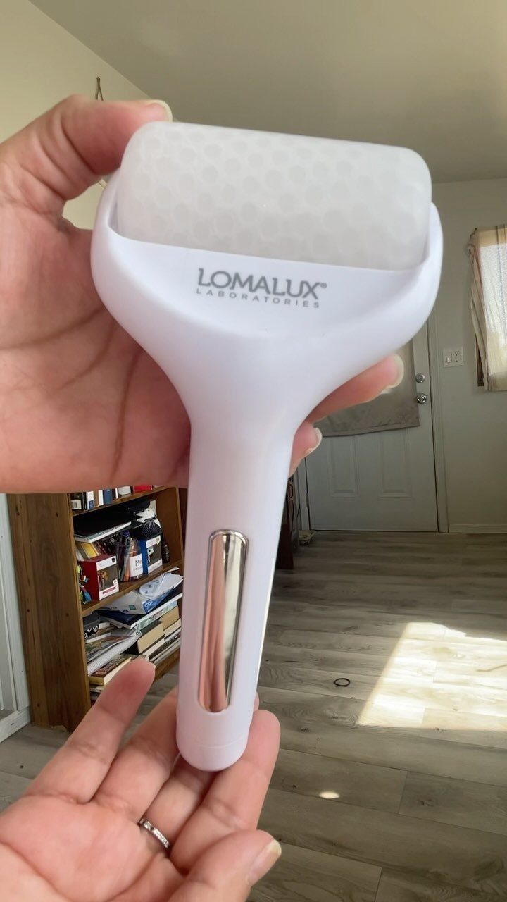 White Lomalux ice roller held in hands against a blurred home interior background.