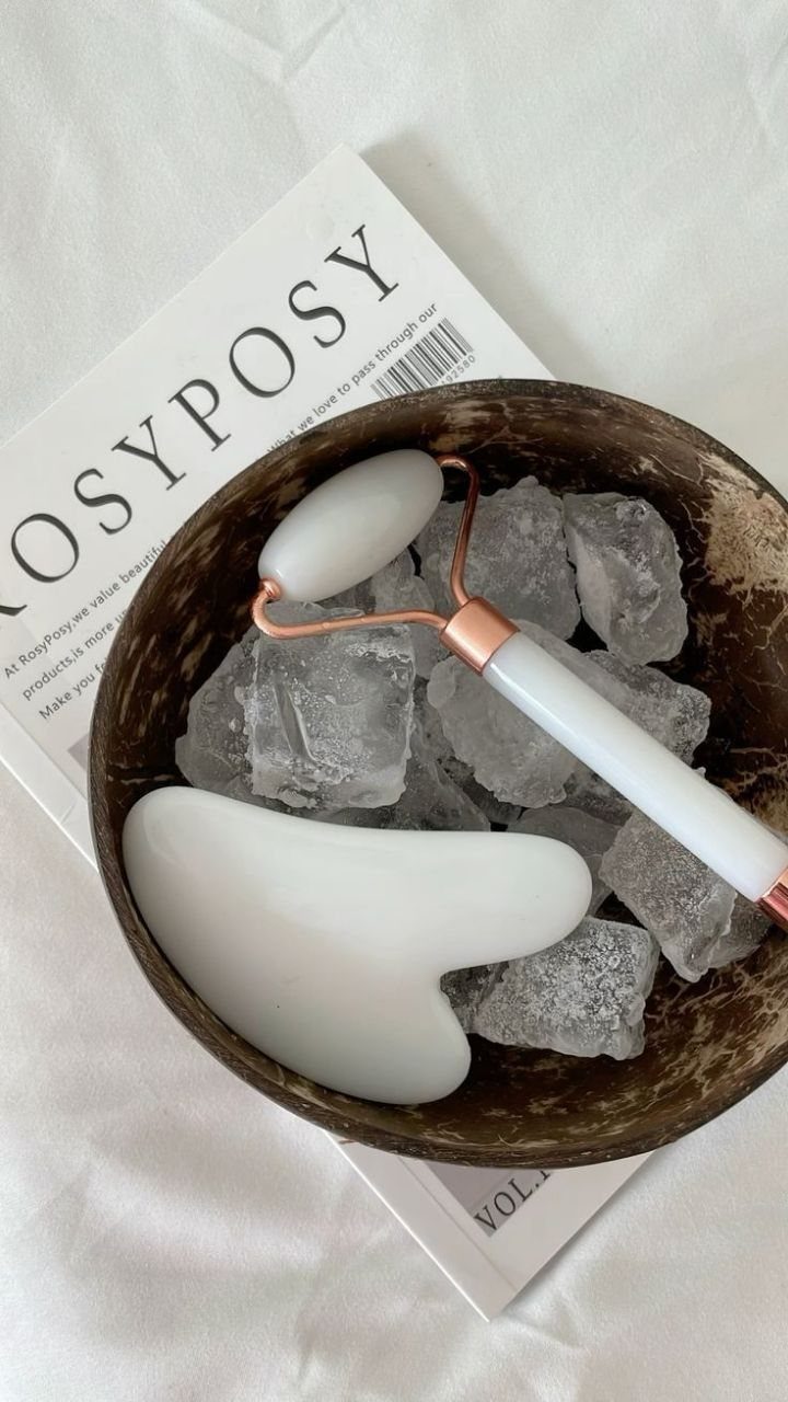 Jade facial roller and gua sha tool chilled on ice in a coconut bowl