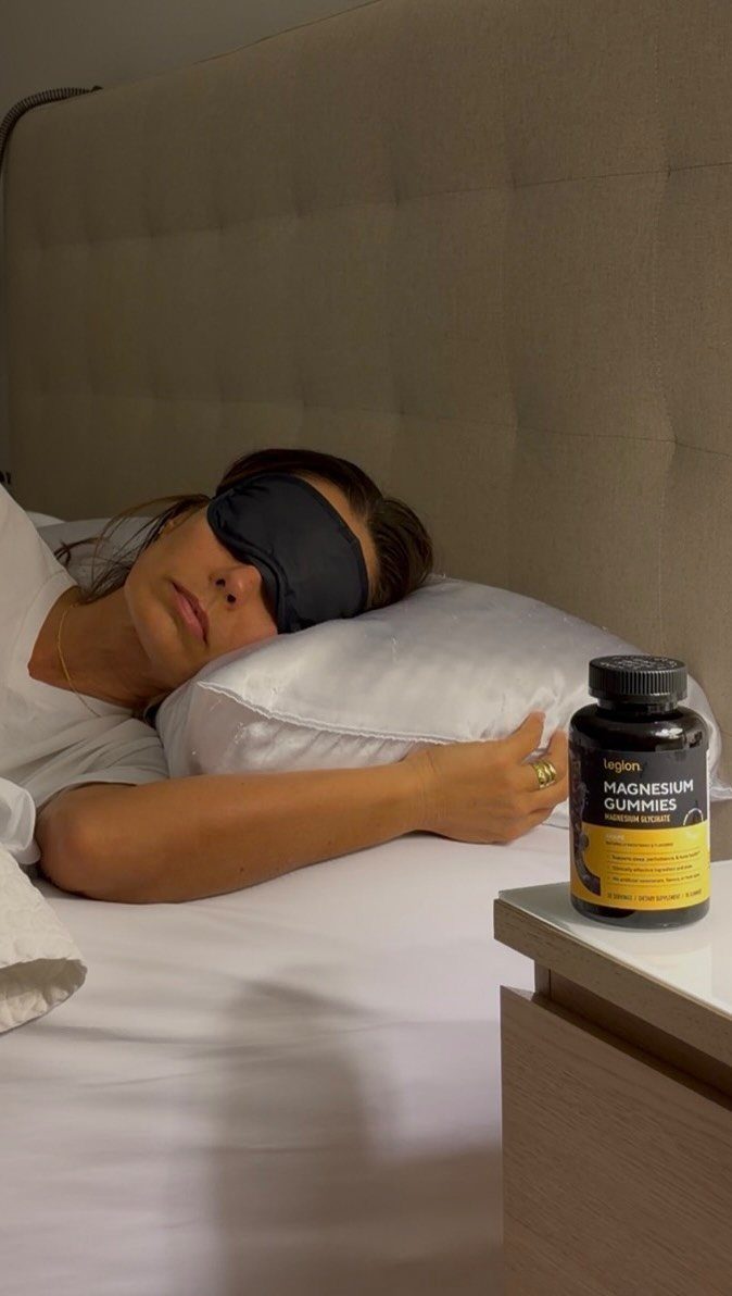 Woman sleeping with a sleep mask next to a bottle of magnesium gummies.